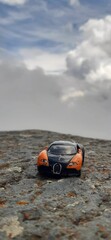Small sports toy car parked atop a large, craggy rock formation, against a mountainous landscape