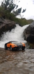 Small sports toy car parked atop a large, craggy rock formation, against a waterfall