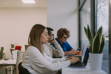 Inter-generational coworkers loosing their focus at the end of the working shift. Girl almost felt asleep on her lap top while her middle-aged colleagues are scrolling on the phone