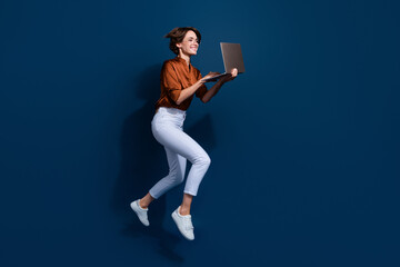 Fototapeta na wymiar Full length photo of sweet excited girl dressed brown shirt jumping working modern gadget empty space isolated blue color background