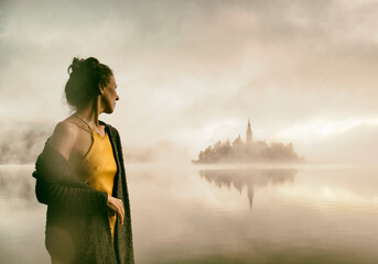 Woman in gray coat watching a sunrise among the fog on the shores of Lake Bled, Slovenia IV