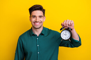 Photo of cheerful energetic man dressed green stylish clothes holding clock isolated on yellow color background - obrazy, fototapety, plakaty