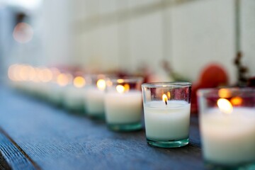 Lit candles and flowers line a shelf on a table outdoors