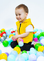 A young boy sitting on a pile of balloons. A Joyful Youngster Surrounded by Colorful Floating Objects