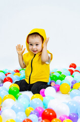 Fototapeta na wymiar A little boy sitting in a ball pit with his hands up. Little Boy's Joyful Adventure in Colorful Ball Pit