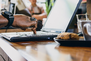 hand of unrecognizable black man touching with one finger laptop keyboard on table inside restaurant