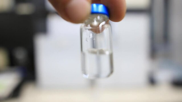 A close up from a man holding a vial with clear water inside a analytical chemistry laboratory