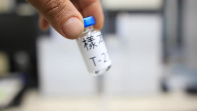 A close up from a man holding a vial with a liquid labelled as sample in Chinese characters inside a analytical chemistry laboratory