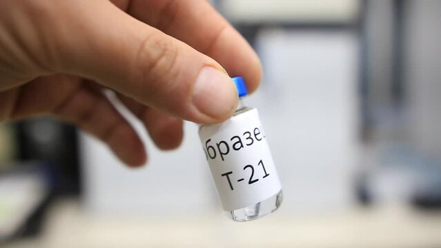 A close up from a man holding a vial with a liquid labelled as sample in russian characters inside a analytical chemistry laboratory