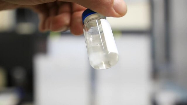 A close up from a man holding a vial with a liquid labelled as sample in chinese characters inside a analytical chemistry laboratory
