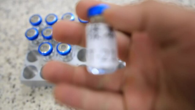 A close up from a man picking up a vial with a liquid labelled as sample in chinese inside a analytical chemistry laboratory