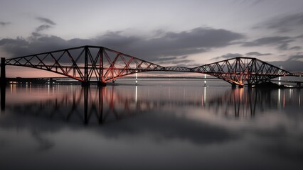 Aerial view of the Forth Bridge, spanning a river and illuminated with red lights at night