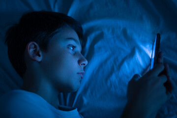 Boy using a smartphone at night in bed. 10 year old boy playing with mobile phone before going to...