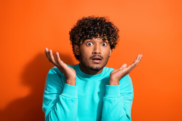 Portrait of confused indian guy raised hands up shrug shoulders unhappy questioned who steal his car isolated on orange color background