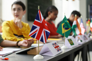Group of international students sitting at table with flags and having lesson at school