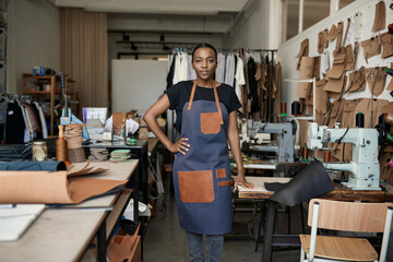 Confident young African female leather worker standing by a sewing machine