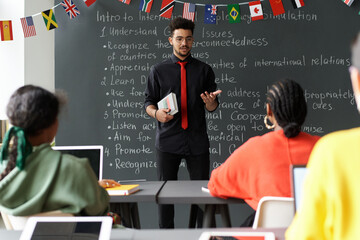 Young teacher standing near the blackboard and having lesson with students in the classroom
