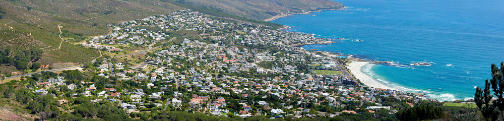 Fototapeta na wymiar Panoramic landscape of a large city on the coast from above. Beautiful scenic and aerial view of a popular tourist town or residential area with greenery and the ocean in nature during summer