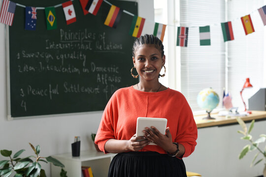 Portrait of African American woman smiling at camera while standing in the classroom and using tablet pc
