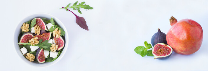 Salad with arugula, feta cheese, fig, walnut in the white bowl and fruit on the white background. Copy space.