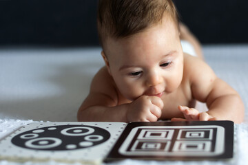 A baby looks at a black and white contrast educational book. Intellectual development of newborns. Developing cards for children. - obrazy, fototapety, plakaty