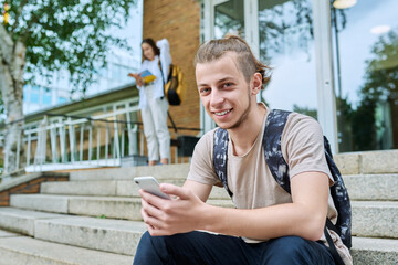 Guy teenager student with backpack using smartphone, outdoor