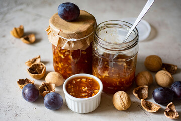 Plum jam with walnuts in a glass jar on a gray background. Close-up