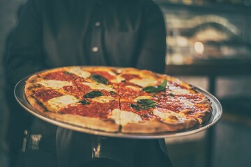 Closeup of a chef holding a pizza on a metal tray