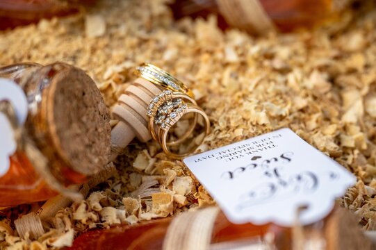 Close-up image of two golden wedding rings sitting on a wooden surface surrounded by two honey jars