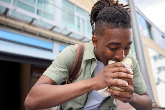 Young Man Eating Burrito At Outdoor Takeaway Street Food Stall