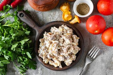 A hearty lunch for the whole family: fried chanterelles with sour cream in a beautiful plate on a gray background. Fried mushrooms with sour cream for lunch. Close-up