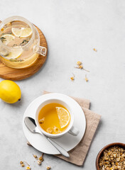 Chamomile herbal tea with lemon in a white cup and teapot with flowers on a light background. The concept of a healthy detox drink for health and sleep.