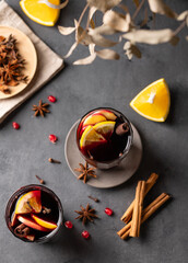Mulled wine with orange, apple and cinnamon in glasses on a dark background. The concept of a traditional winter hot drink with spices and fruits for the holiday.