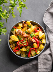 Fried pork meat with potatoes, onions and peppers. National homemade Georgian dish ojakhuri in a bowl on a dark background with fresh herb and napkin.
