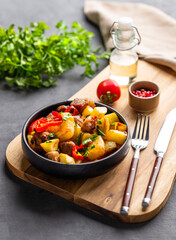 Fried pork meat with potatoes, onions and peppers. National homemade Georgian dish ojakhuri in a black bowl on a wooden board on a dark background