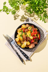 Fried pork meat with potatoes, onions and peppers. National homemade Georgian dish ojakhuri in a black bowl on a yellow background with fresh herb and shadows.
