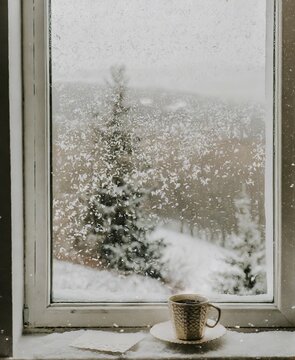 Cup of coffee on window, while there's snowing outside