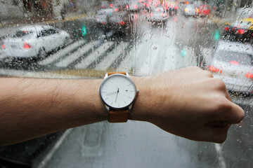 A man's point of view as he checks time on his watch. In the background, a raindrop window and...