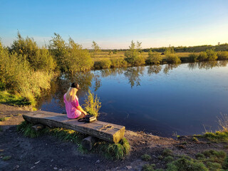 Kobieta blond siedząca nad jeziorem na ławce.