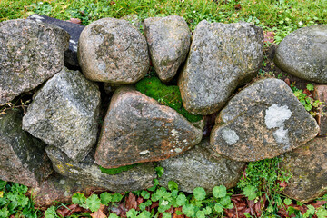 Background. Nature background of a rock garden wall outside on a sunny day with delicate moss and plants growing between the stones. Wallpaper of structural support barrier fencing in a garden.