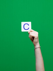 Lettre en carton et bois tenue par une main d'enfant sur fond vert détourage facile pour création...