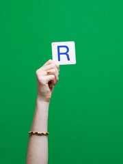 Lettre en carton et bois tenue par une main d'enfant sur fond vert détourage facile pour création...