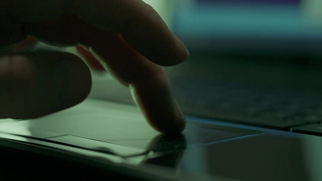 Close-up of the hands of a hacker programmer working with the mouse and keyboard of a portable laptop laptop in a dark room. Freelancer using laptop. Moves a finger across the touchpad of a laptop