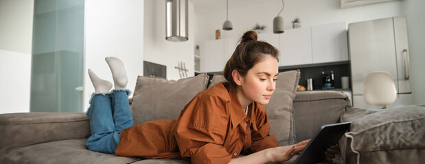 Weekend and lifestyle concept. Young woman lying on couch with digital tablet, scrolling social...