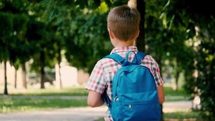 Junior schoolboy dressed in checkered shirt walks to school through city park