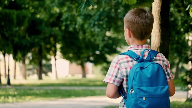 Junior schoolboy dressed in checkered shirt walks to school through city park