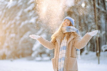 A young woman throws out snow. Portrait of a happy woman playing with snow on a sunny winter day. A walk through the winter forest. Concept of fun, relaxation. - obrazy, fototapety, plakaty