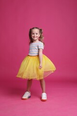 Cute little girl in tutu skirt dancing on pink background