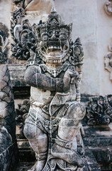 Ancient balinese stone statue depicting a fierce guardian deity, adorned with intricate carvings, stands vigilant at a temple.