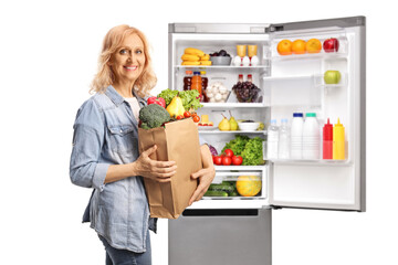 Mature woman with a grocery bag next to an open fridge with food